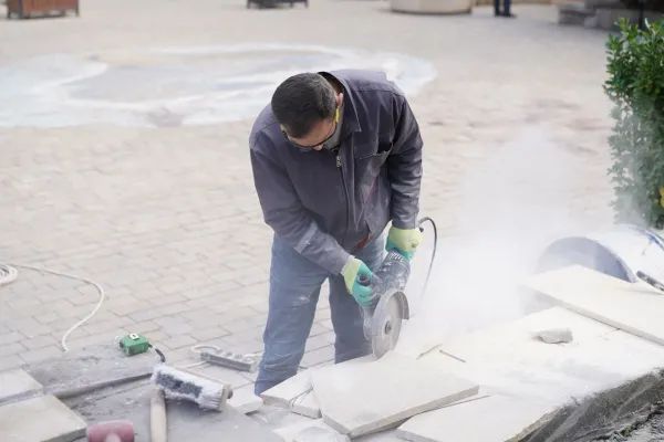 A worker cutting stone pavers with a power saw for an outdoor paving job