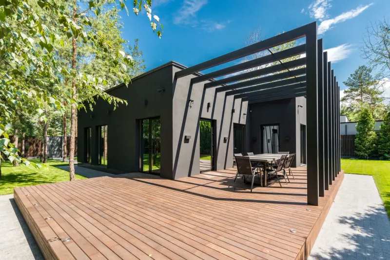 A new timber deck and pergola beside a modern house, with a lawn and planted border